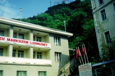 Gjirokastër – gatubild full av politisk propaganda:  ”PARTI – ENVER” står det längst upp på höjden; på huset kan man läsa något om marxism-leninismen; under de röda fanorna kan man läsa om BPSH:s kongress (BPSH var något slags fackförening).